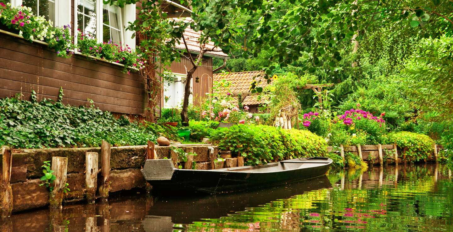 Kleine Ferienhaeuser in der Naehe der Spree mit einem Boot auf dem Fluss | © Gettyimages.com/kerrick