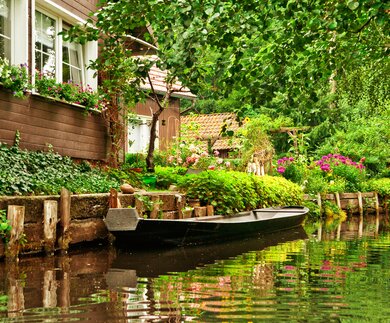 Kleine Ferienhaeuser in der Naehe der Spree mit einem Boot auf dem Fluss | © Gettyimages.com/kerrick