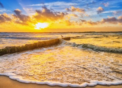 Wunderschoener Herbstsonnenuntergang am Hauptstrand von Westerland mit einer Moewe, die auf einem Wellenbrecher sitzt. Wellen plaetschern an den Strand. | © Gettyimages.com/Juergen Sack