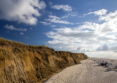 Links sieht man eine steile Klippe. Rechts Strandkörbe und Menschen am Strand | © Gettyimages.com/viktorkunz
