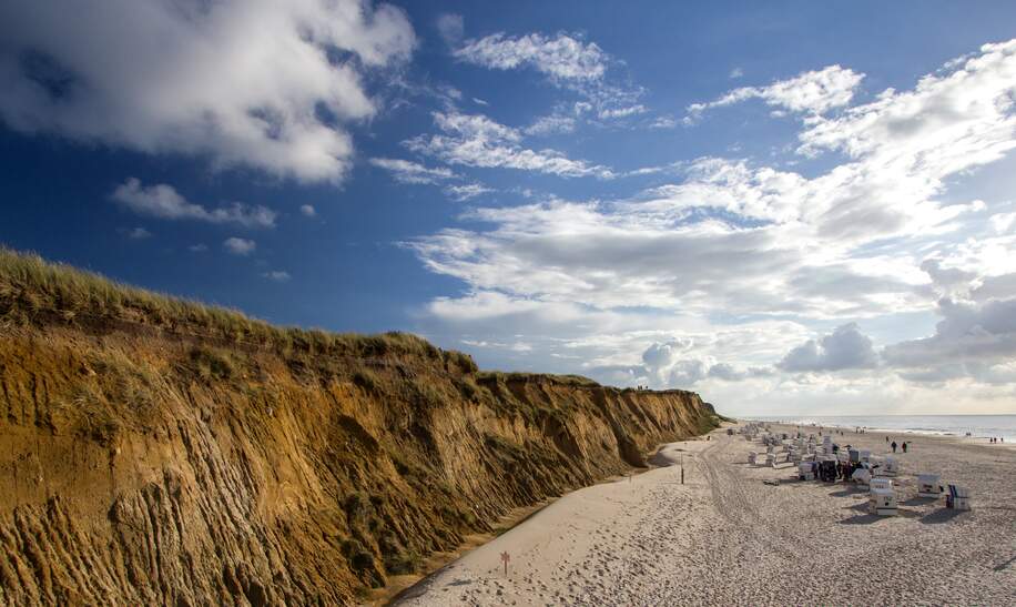 Links sieht man eine steile Klippe. Rechts Strandkörbe und Menschen am Strand | © Gettyimages.com/viktorkunz