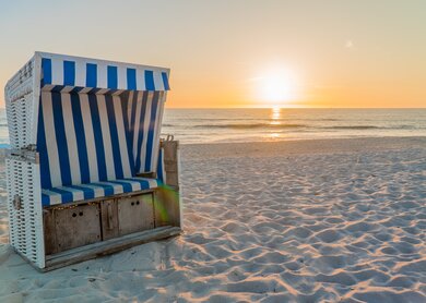 Blau-weiß gestreifter Strandkorb bei Sonnenuntergang auf Sylt | © Gettyimages.com/undefined undefined