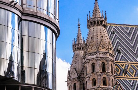 Der mittelalterliche Stephansdom in Wien mit seinem markanten Mosaik-Ziegeldach existiert gegenüber einem modernen Bürogebäude mit abgerundeten Glasfenstern | © Gettyimages.com/KenWiedemann