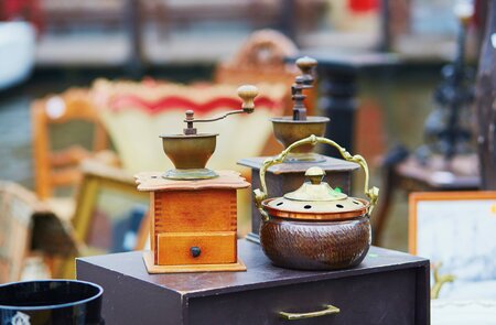 Auf einem Flohmarkt in Brügge stehen Antiquitäten wie eine alte Kaffeemühle und eine Teekanne.  | © Gettyimages.com/encrier