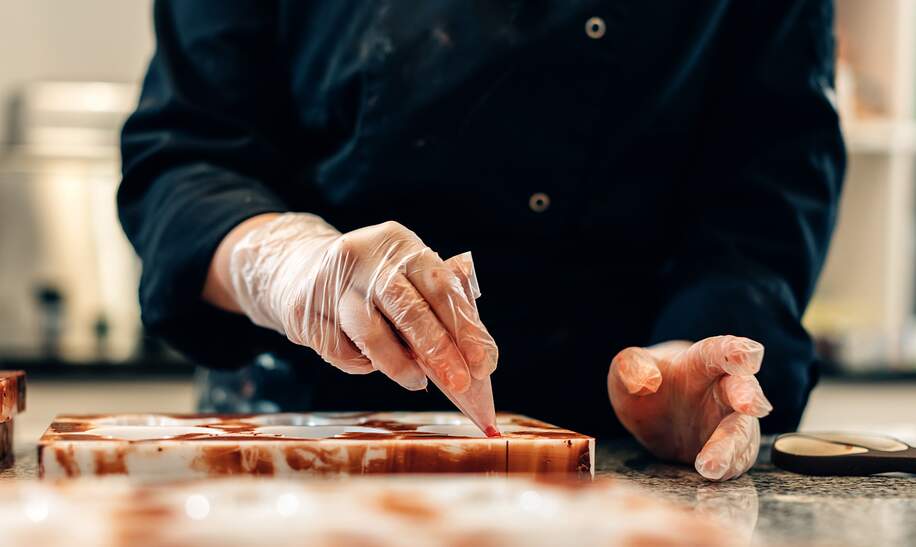 Nahaufnahme der Hände eines Konditors, der weiße Pralinen in einer handwerklichen Werkstatt schmückt, Brüssel | © Gettyimages.com/Carlo Prearo