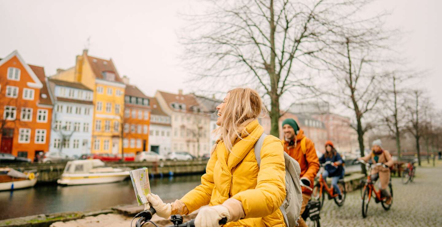 Gruppe Touristen mit dicken Jacken und Mützen auf Fahrrädern am Hafen in Kopenhagen, Dänemark, vor den berühmten Nyhavn | © GettyImages.com/AleksandarNakic