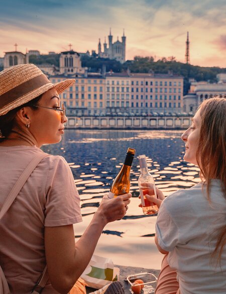 Zwei glückliche Mädchen trinken Wein aus Flaschen und beobachten eine Sonne geht über Saone Fluss in Lyon  | © Gettyimages.com/frantic00
