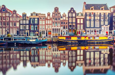 Amsterdams traditionelle Häuserarchitektur mit Hausbooten spiegelt sich am frühen Morgen in einer Gracht | © Gettyimages.com/KavalenkavaVolha