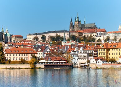 Prager Burg mit orangefarbenen Dächern historischer Gebäude von Mala Strana, die sich an einem hellen Sommertag in Prag im Flusswasser spiegeln. | © Gettyimages.com/anyaivanova