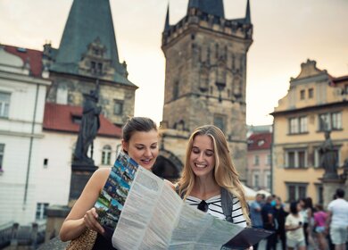 Junge Frauen stehen auf der Karlsbrücke und erkunden die Stadt mit Stadtplan in Prag. | © Gettyimages.com/kamisoka