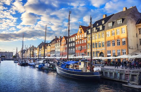Bunte historische Häuser am Nyhavn in Kopenhagen spiegeln sich im Wasser, Segelboote liegen am Kai unter blauem Himmel mit Wolken bei Sonnenuntergang. | © Gettyimages.com/	AleksandarGeorgiev