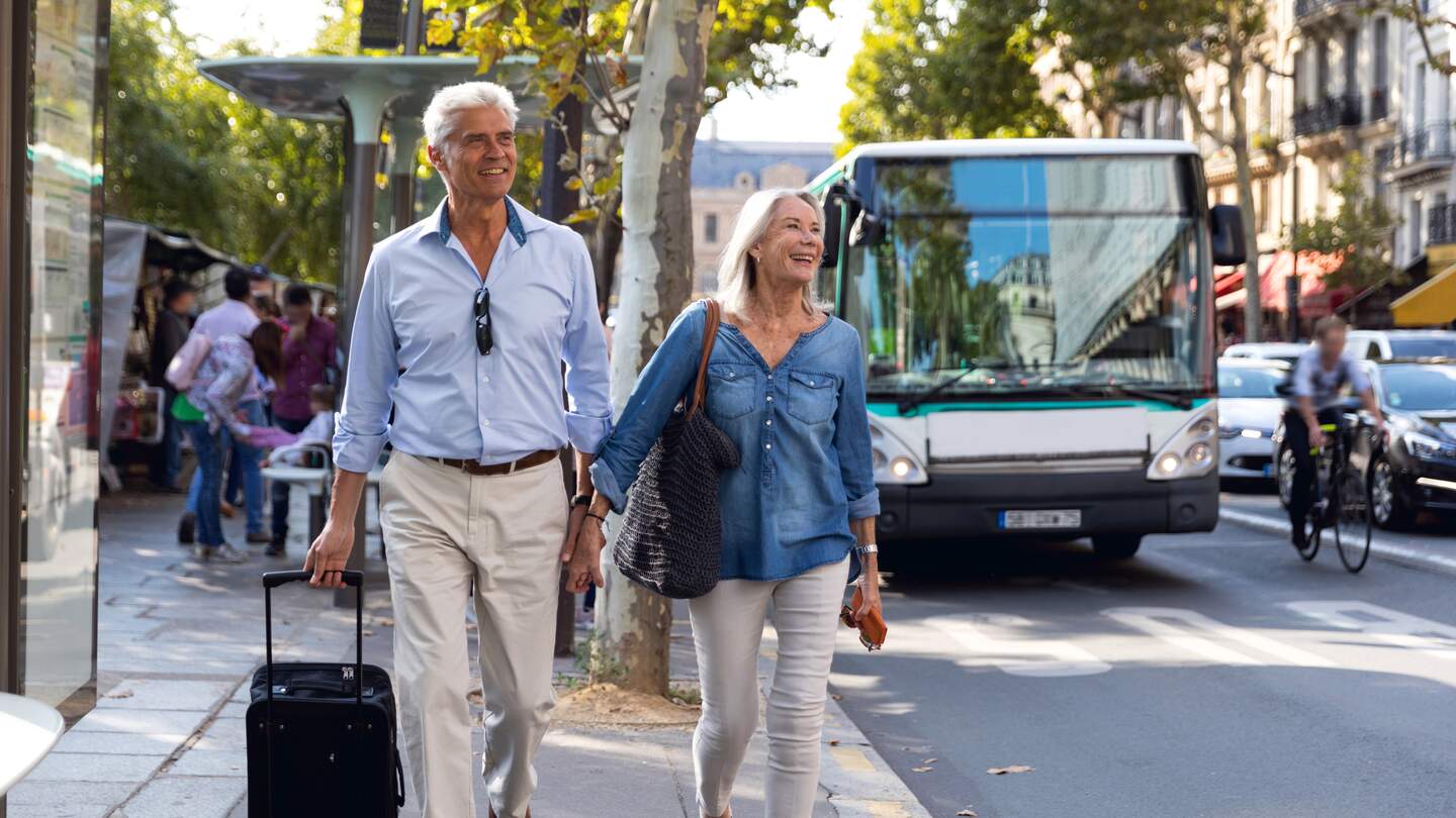 Seniorenpaar, das händehaltend vor dem Bus in Paris läuft. | © Gettyimages.com/LeoPatrizi