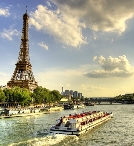 Menschen machen eine Bootsfahrt auf der Seine in Paris, Lastkähne und Bäume bei Sonnenuntergang. | © Gettyimages.com/AleksandarGeorgiev