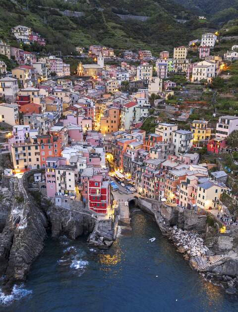 Luftaufnahme von Riomaggiore in der Cinque Terre, Italien, bei Abenddämmerung. Die charakteristischen bunten Häusern und der Hafen sind von den steilen Weinbergen und dem Ligurischen Meer umgeben. | © Gettyimages.com/Paolo Graziosi