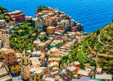 Luftaufnahme von Manarola im Cinque Terre Nationalpark, umgeben von Weinbergen und mit dem Ligurischen Meer im Hintergrund an einem sonnigen Sommertag. | © Gettyimages.com/Eloi_Omella