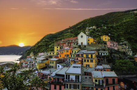 Farbenfrohe Luftaufnahme des Dorfes Vernazza in der Cinque Terre, Italien, mit Blick auf die bunten Häuser, das Ligurische Meer und die umliegenden Berge im warmen Licht des Sonnenuntergangs. | © Gettyimages.com/serts