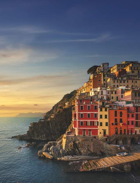 Blick vom Meer auf das Dorf Riomaggiore in der Cinque Terre, Italien, mit den charakteristischen bunten Häusern und dem Hafen in den warmen Farben des Sonnenuntergangs. | © Gettyimages.com/StevanZZ