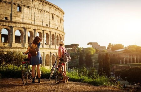 Zwei Freundinnen mit Fahrraedern vor dem Kolosseum in Rom und geniessen die warme Nachmittagssonne | © gettyimages.com/piola666