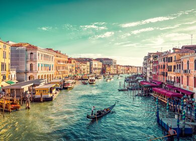 Ein Gondelfahrer paddelt in Richtung des Sonnenuntergangs auf dem grossen Kanal von Venedig. Aufnahme von der Rialto-Bruecke | © Gettyimages.com/JaCZhou