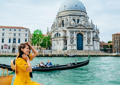 Frau im gelben Sonnenkleid sitzt am Ufer mit Blick auf den großen Kanal in Venedig. | © Gettyimages.com/Vera_Petrunina