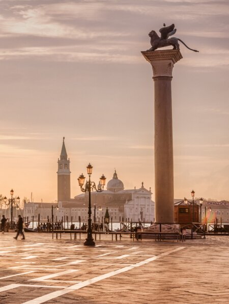Auf dem Markusplatz in Venedig laufen Menschen. Die Sonne scheint durch den Dogenpalast. | © Gettyimages.com/tunart