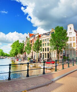 Blick auf die Amstel und eine Bruecke mit einer historischen Strassenlaterne im linken Vordergrund | © Gettyimages.com/adisa