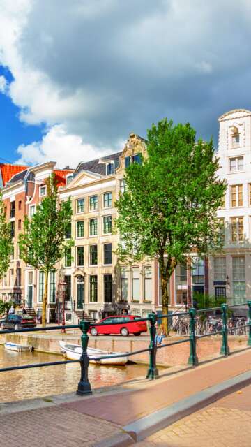Blick auf die Amstel und eine Bruecke mit einer historischen Strassenlaterne im linken Vordergrund | © Gettyimages.com/adisa