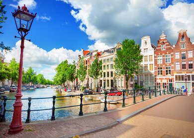Blick auf die Amstel und eine Bruecke mit einer historischen Strassenlaterne im linken Vordergrund | © Gettyimages.com/adisa
