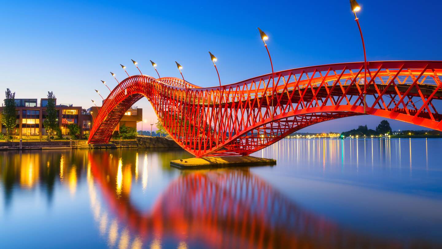Die abendlich kunstvoll beleuchtete Fußgaengerbrücke Python Bridge, auch High Bridge genannt, in Amsterdam spiegelt sich im Kanal | © Gettyimages.com/Biletskiy_Evgeniy