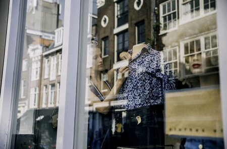 Junge Schaufenster-Dekorateurin in Amsterdam fixiert eine gemusterte Bluse auf einer Bueste | © Gettyimages.com/SolStock
