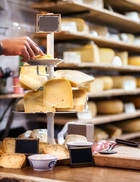 Eine Frau probiert und wählt Bio-Käse von einer Etagere aus vielen Käsesorten in einem Kaesegeschaeft mit in Amsterdam  | © Gettyimages.com/guruXOOX