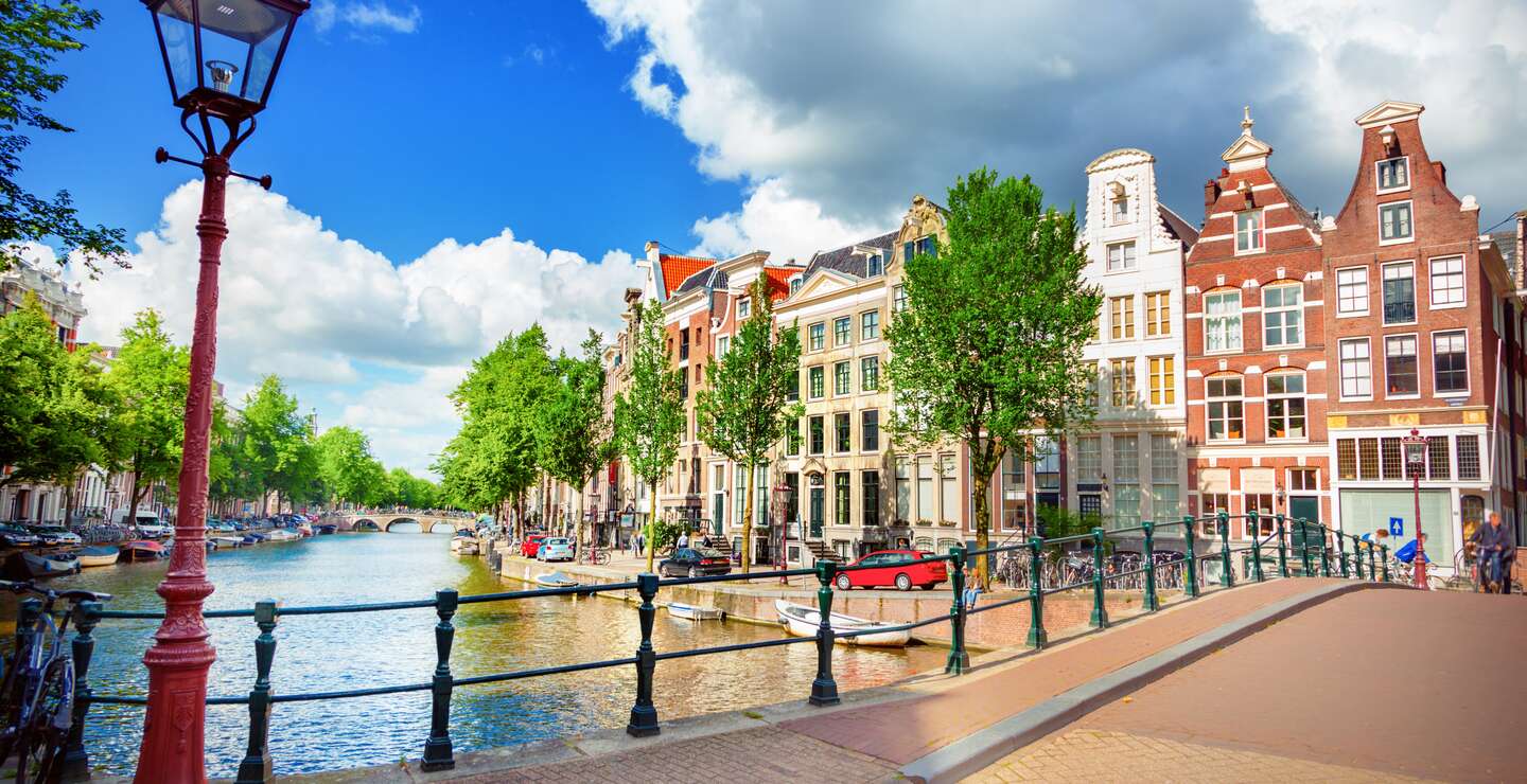 Blick auf die Amstel und eine Bruecke mit einer historischen Strassenlaterne im linken Vordegrund | © Gettyimages.com/adisa