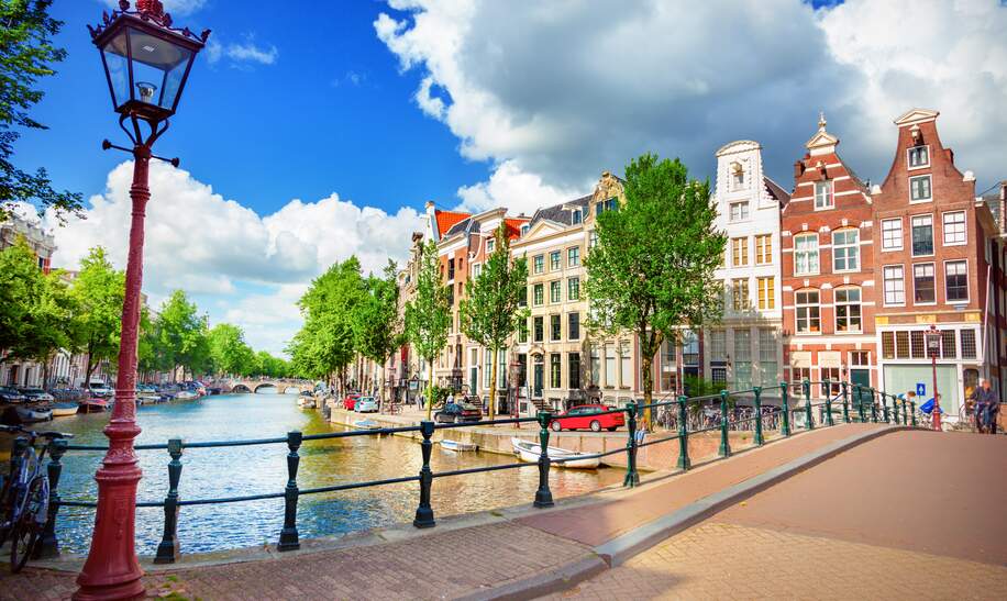 Blick auf die Amstel und eine Bruecke mit einer historischen Strassenlaterne im linken Vordegrund | © Gettyimages.com/adisa