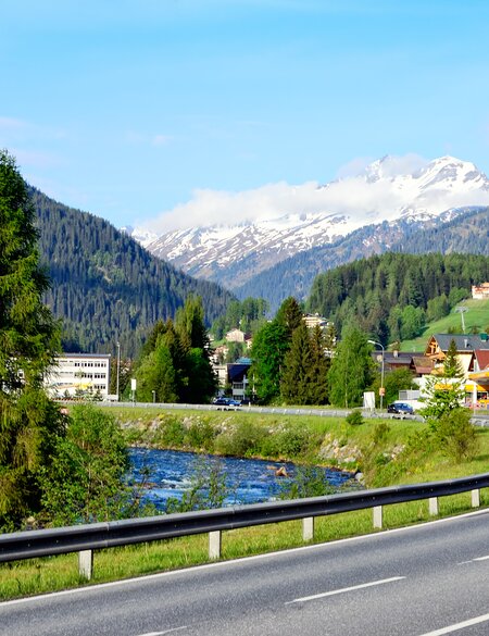 Blick auf Sankt Anton in Österreich an einem sonnigen Sommertag, umgeben von grünen Wiesen und den majestätischen Alpen. | © Gettyimages.com/alxpin