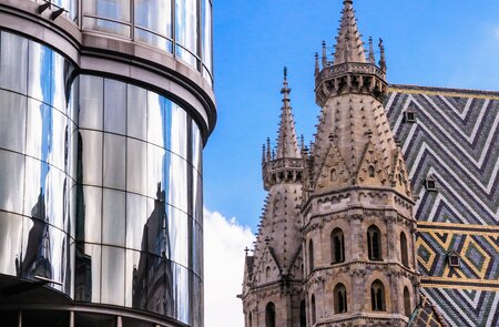 Der mittelalterliche Stephansdom in Wien mit seinem markanten Mosaik-Ziegeldach existiert gegenueber einem modernen Buerogebaeude mit abgerundeten Glasfenstern | © Gettyimages.com/KenWiedemann