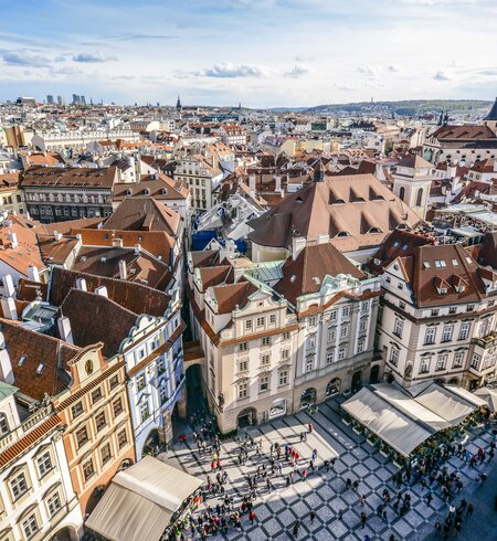 Luftaufnahme über die orangefarbenen Daecher des Altstaedter Rings in Prag, Touristen stehen auf dem Platz im Vordergrund. | © Gettyimages.com/AleksandarGeorgiev