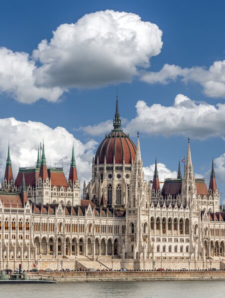 Schraegansicht der Aussenfassade des ungarischen Parlamentsgebaeudes in Budapest an der Donau mit blauem Himmel und Schoenwetterwolken | © GettyImages.com/Frank Wagner