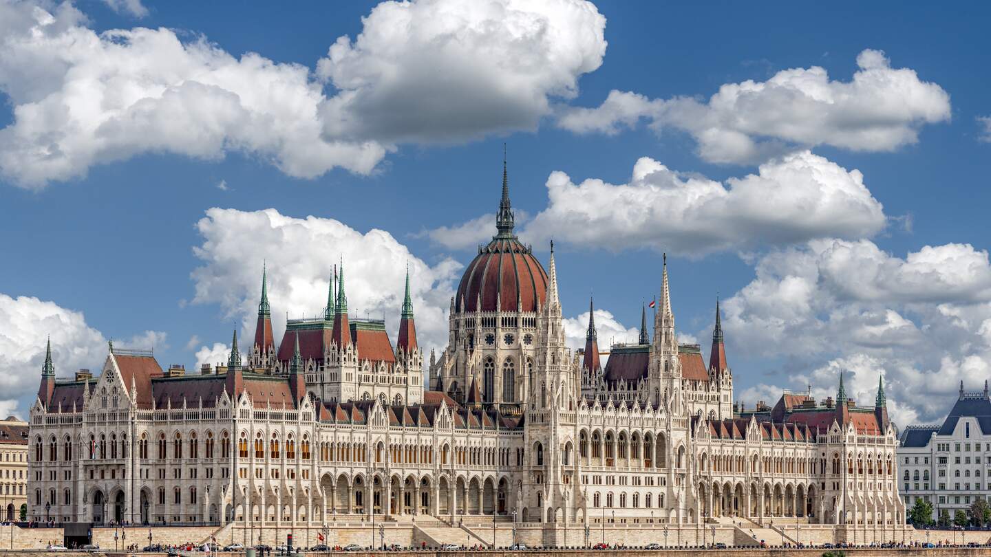 Schraegansicht der Aussenfassade des ungarischen Parlamentsgebaeudes in Budapest an der Donau mit blauem Himmel und Schoenwetterwolken | © GettyImages.com/Frank Wagner