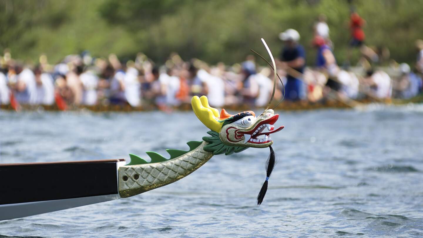 Bunt verzierter Bug eines Drachenbootes während eines Rennens auf einem See mit vielen Zuschauer  | © Gettyimages.com/EasyBuy4u