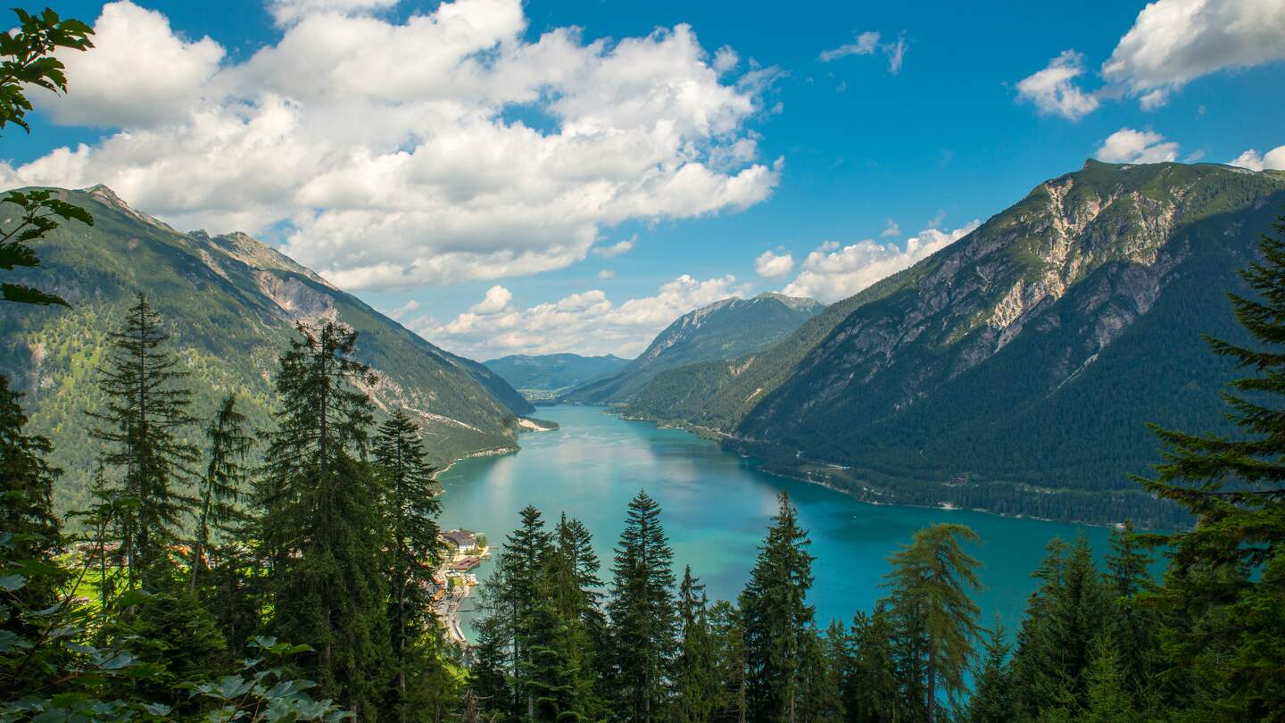Ein klarer blauer See liegt eingebettet zwischen grünen Berghaengen unter einem Himmel mit weissen Wolken. | © gettyimages.com/mytrade1