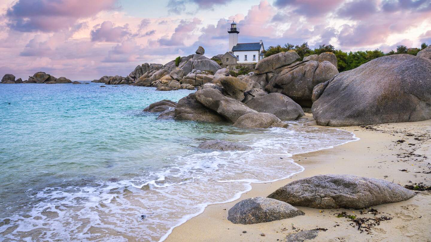 Der Leuchtturm Pontusval, der sich auf einem felsigen Punkt im noerdlichen Finistere in der Bretagne befindet, ueberblickt waehrend des Sonnenaufgangs ein Meer aus transparentem tuerkisfarbenem Wasser. | © Gettyimages.com/fedevphoto