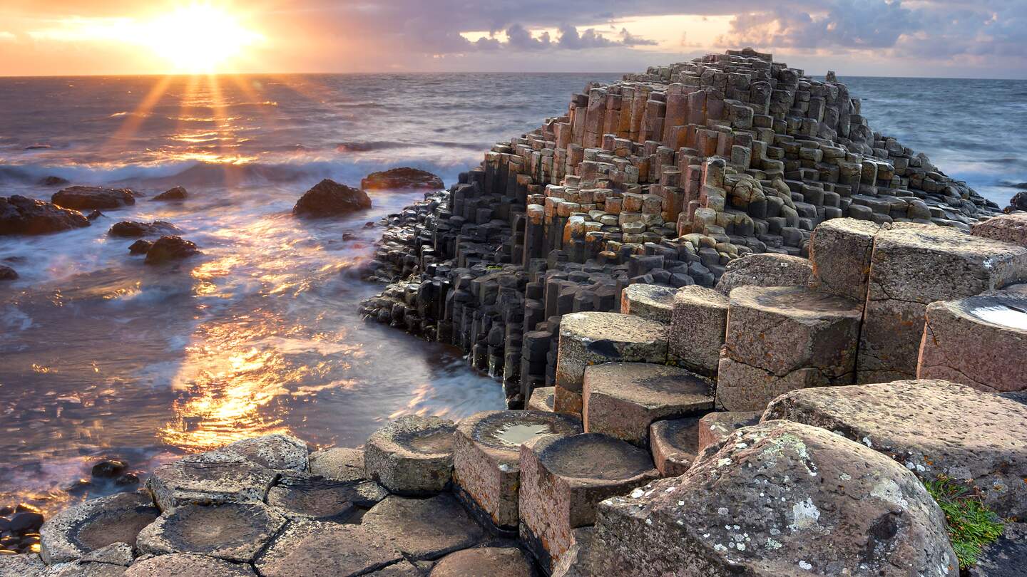 Besucher des Giant s Causeway bei Sonnenuntergang in North Antrim, Nordirland | © Gettyimages.com/aitormmfoto