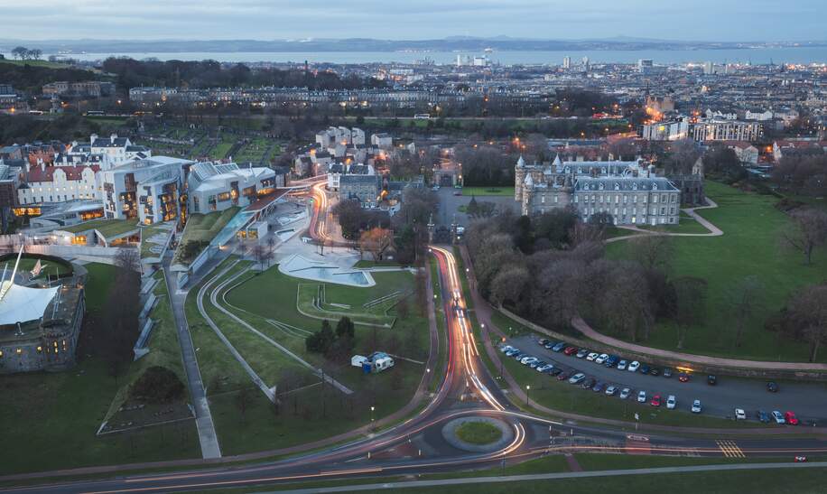 Ein atemberaubender Abendblick von Salisbury Crags über die moderne Architektur des schottischen Parlamentsgebaeudes gegenueber dem Holyrood Palace am Fusse der Royal Mile in Edinburgh, Schottland. | © Gettyimages.com/stephenbridger