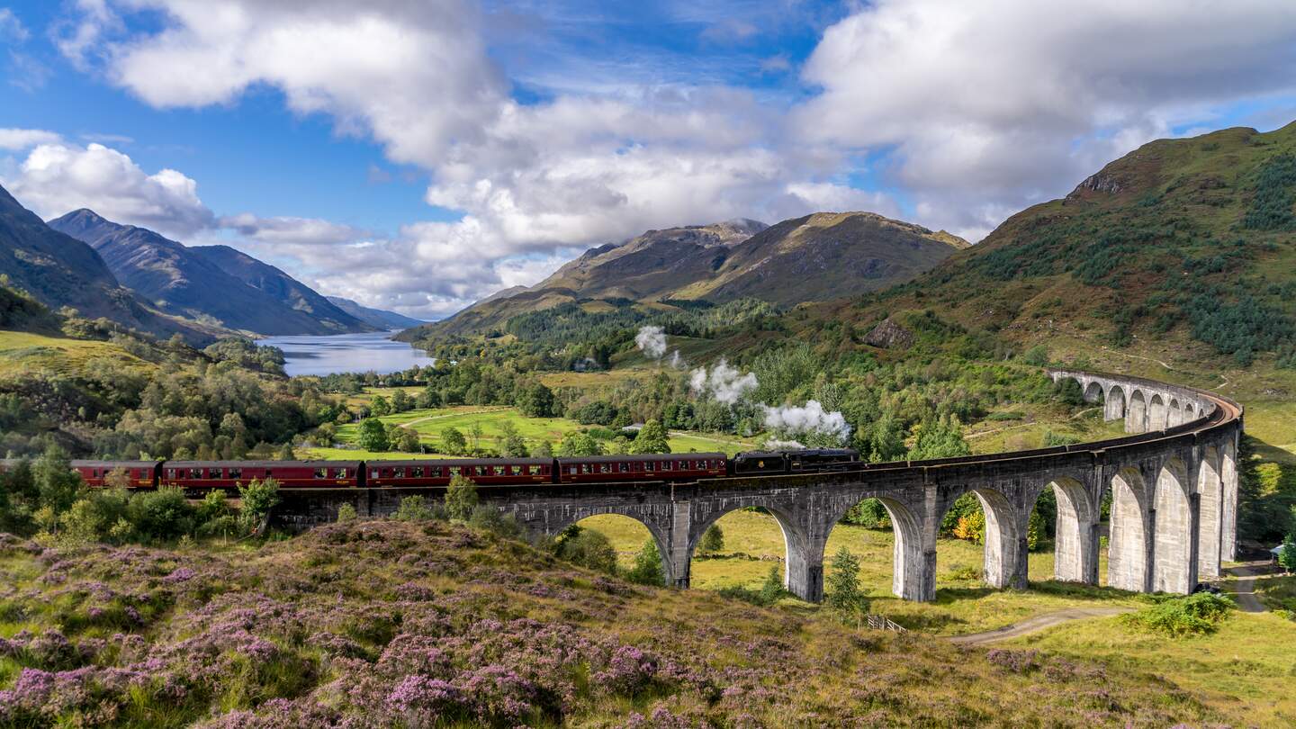 Beruehmten Glenfinnan Eisenbahnviadukt in Schottland. Ein Zug faehrt gerade ueber das gigantische Bauwerk mit atemberaubenden Hintergrund | © Gettyimages:com/catuncia