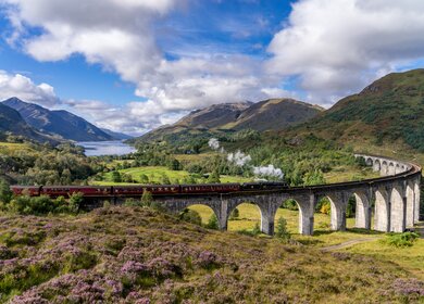 Berühmten Glenfinnan Eisenbahnviadukt in Schottland. Ein Zug fährt gerade über das gigantische Bauwerk mit atemberaubenden Hintergrund | © Gettyimages:com/catuncia