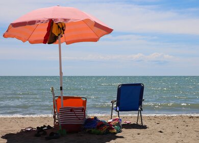 Blauer und oranger Liegestuhl mit orangem Sonnenschirm direkt am Meer | © Gettyimage/ChiccoDodiFC