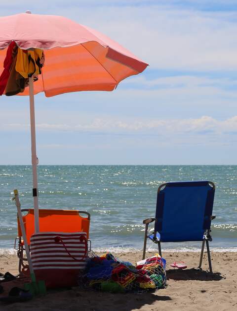 Blauer und oranger Liegestuhl mit orangem Sonnenschirm direkt am Meer | © © Gettyimage/ChiccoDodiFC