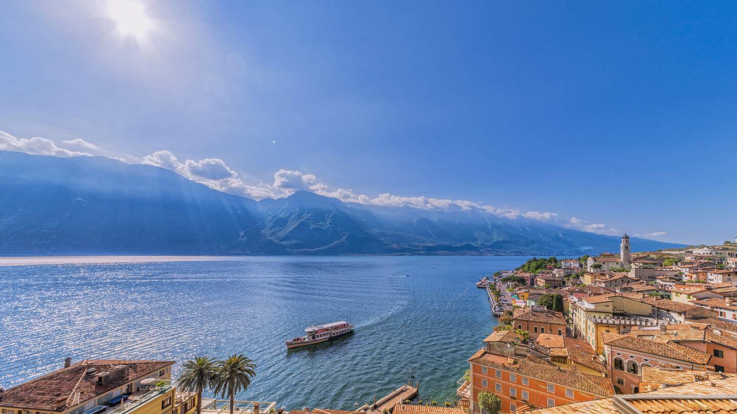  schoene Aussicht auf den Gardasee und die berühmte Stadt Limone sul Garda an einem schönen Fruehsommertag. Eine Faehre naehert sich von Malcesine | © Gettyimages.com/sack