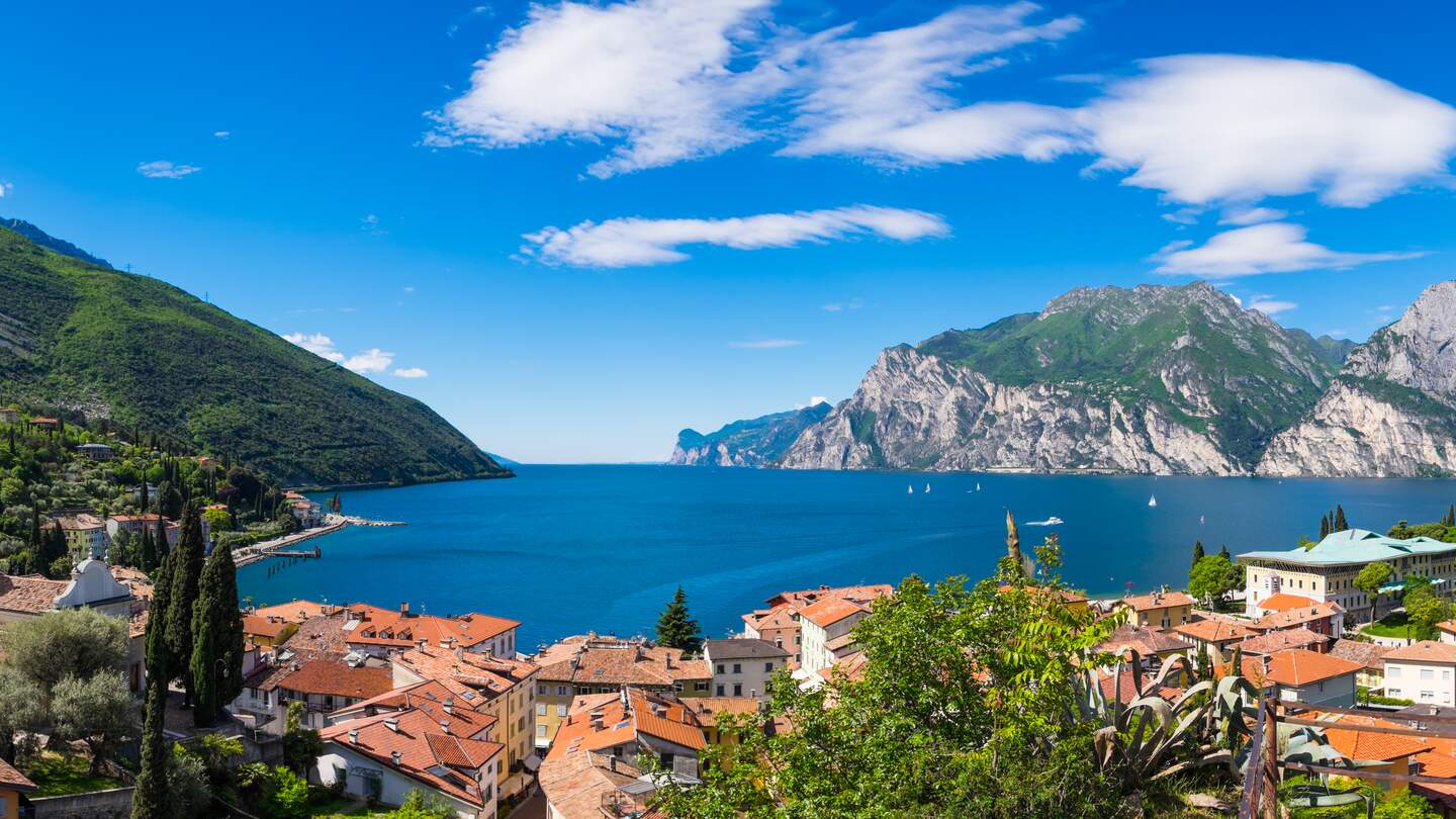 Der Gardasee von der Aaussichz eines Berges aus.Unten ist ein Dorf zu sehen, der Himmel ist blau | © Gettyimages.com/zodebala