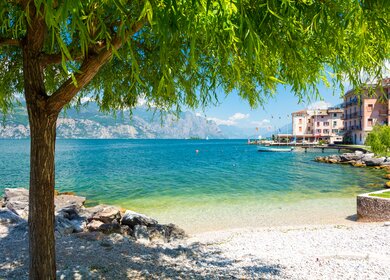 Auf dem Bild sieht man den See mit den felsigen Bergen im Hintergrund. Ein Baum ragt von links in das Bild | © Gettyimages.com/milenapigdanowicz-fidera